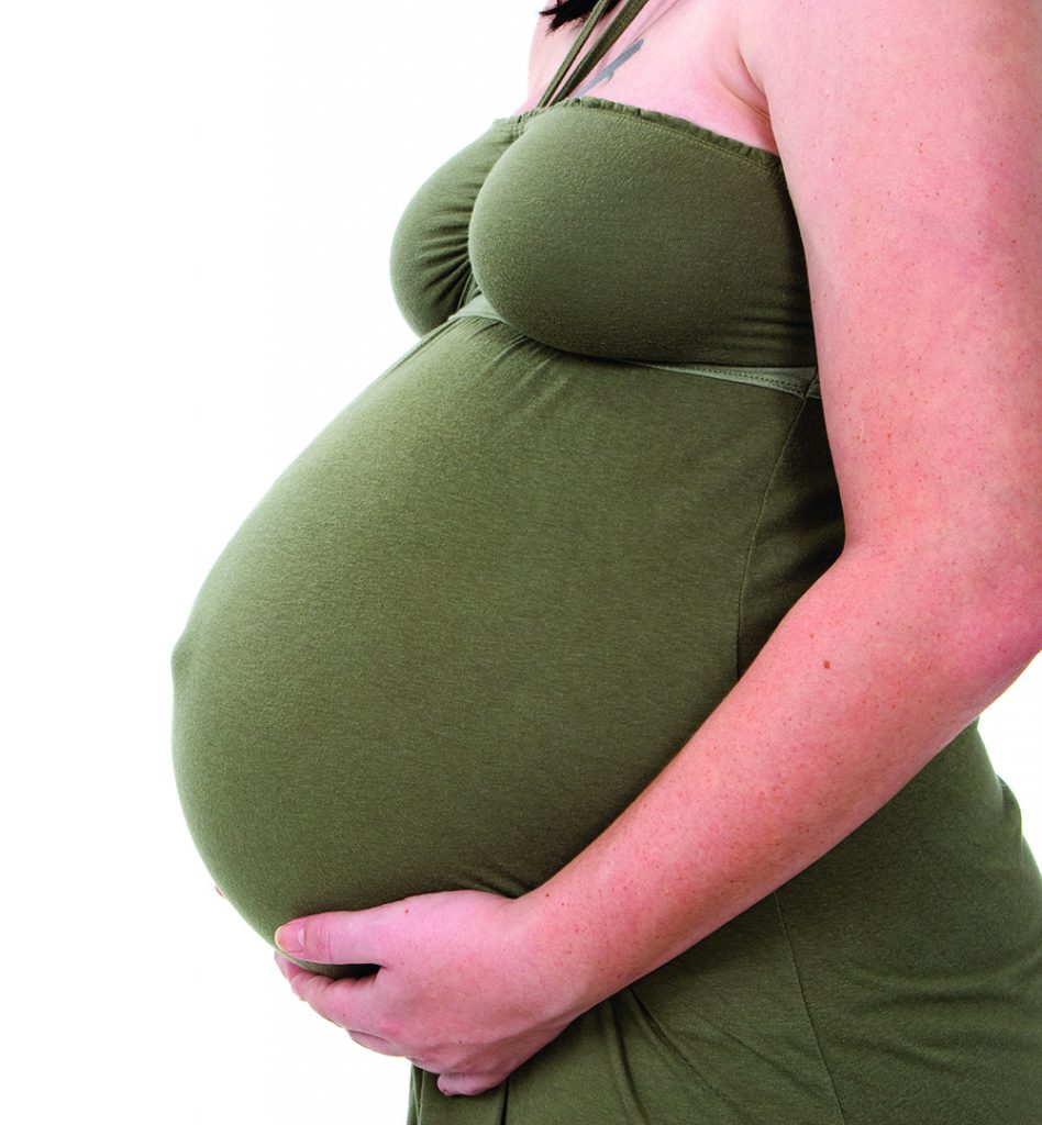 Torso view of a young pregnant woman holding her swollen belly.