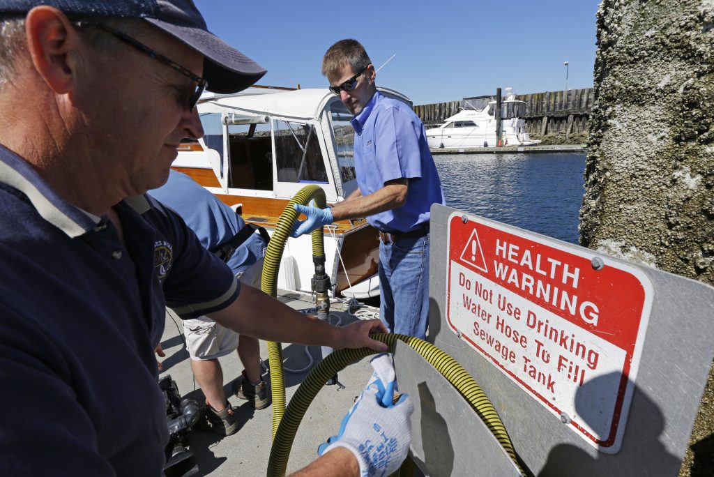 Todd Powell, right, of Federal Way, Wash., helps Pat Wolfrom, left, put away the hose from a sewage pump-out station after Powell demonstrated to reporters how to pump out the sewage holding talk on his boat at the Des Moines Marina, Thursday, July 21, 2016, in Des Moines, Wash. Washington state officials said Thursday that they have petitioned the U.S. Environmental Protection Agency to designate the waters of Puget Sound a "no discharge zone," which would mean boaters and vessel operators would not be able to release sewage, treated or untreated, into Puget Sound. (AP Photo/Ted S. Warren)